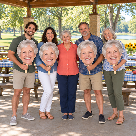 Five adults at a lakeside picnic pavilion, with four holding oversized matching head cutouts of the smiling older woman standing in the center.