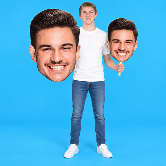 Young adult holding custom big head cutouts: a giant face cutout and a smaller head on a stick against a blue background.